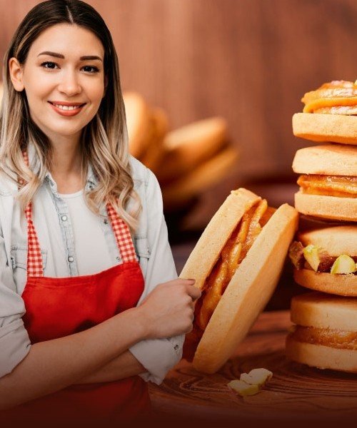 Alfajores apilados con dulce y pistachos junto a una persona con delantal